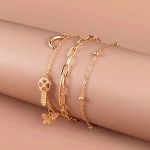 Detailed view of triple gold bracelet set with moon, key and butterfly charms on display