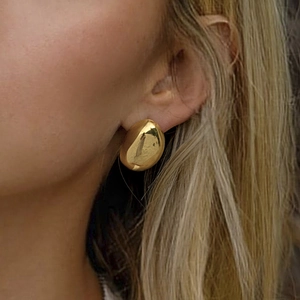 Close-up of golden irregular teardrop stud earrings with mirror polish on a model's ear