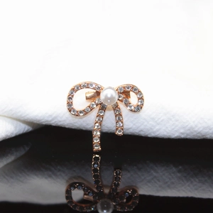 Macro detail of a rose gold bow brooch with sparkling rhinestones and a white pearl