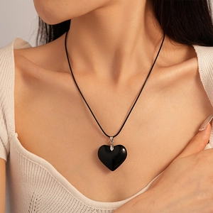 Detail of a vintage black heart pendant on a leather cord worn by a model