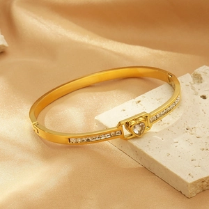 Detailed shot of a gold heart bangle with sparkling zircon stones on a silk background