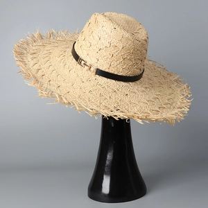 Detail of raffia straw hat featuring frayed edges and black belt with gold buckle