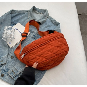 Macro detail of orange quilted nylon chest bag on denim jacket with adjustable strap