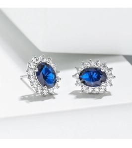 Detailed macro view of sunburst stud earrings with oval blue sapphire and white diamonds