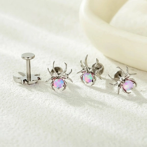 Set of four titanium spider body jewelry studs with pink opal stones on white fabric