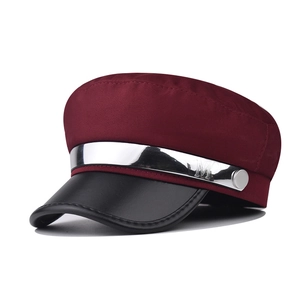 Detail of burgundy newsboy cap featuring silver metal chain and engraved M letter charm
