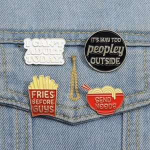 Detailed view of four funny enamel pins featuring text slogans on a denim jacket pocket
