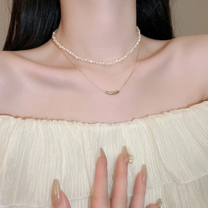 Detail of a double-layered necklace featuring white pearls and a curved gold bar pendant