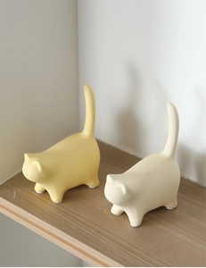 Minimalist ceramic cat ornaments in yellow and cream white on a wooden shelf