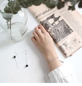 Bracciale a catena box in argento S925 e orecchini con nappe su sfondo di giornale