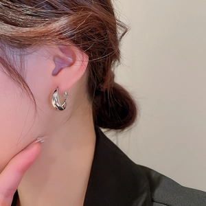 Gros plan d'une créole géométrique torsadée en argent portée par un mannequin chic