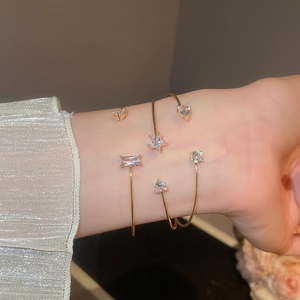 Detail of two gold-plated open bracelets with sparkling zircon star and heart crystals