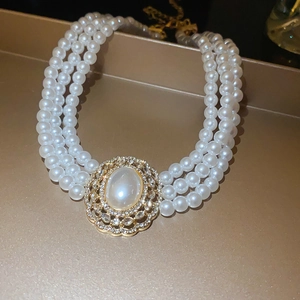 Detail of three-layer pearl necklace with ornate oval pendant in gold finish and rhinestones