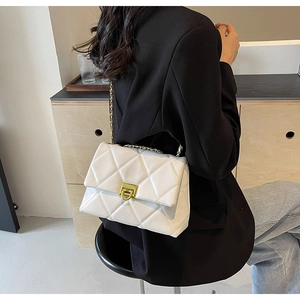 Woman in black blazer wearing a white quilted crossbody bag with gold chain strap