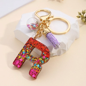 Detail of resin letter R keychain with colorful sequins, purple tassel and gold ring