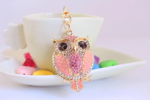 Macro shot of owl keychain with pink rhinestones and enamel on golden metal chain