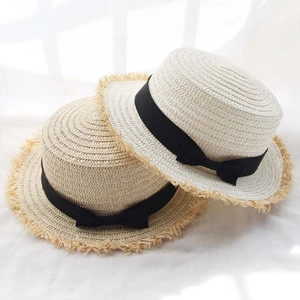 Elegant raffia sun hats in beige and cream with black bows and fringe edges on white background