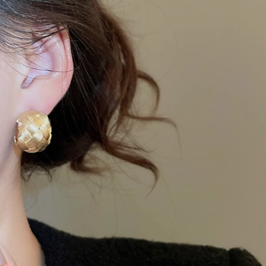 Detailed view of chunky golden C-shaped earring with intricate woven metallic texture