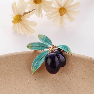 Detailed macro view of an olive-shaped brooch with purple fruit on a beige ceramic plate