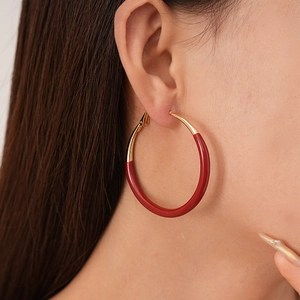 Detail of a large gold and burgundy enamel hoop earring worn by a female model