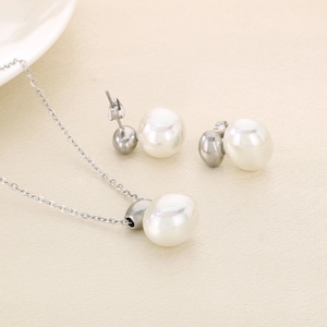 Detailed view of silver necklace and pearl earrings set on beige textured background