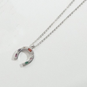 Macro shot of silver horseshoe pendant with multicolored zircon stones on white leather