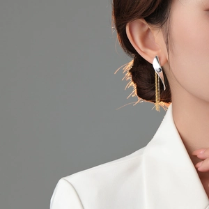 Detailed close-up of mixed metal leaf earring with gold chain tassels on model