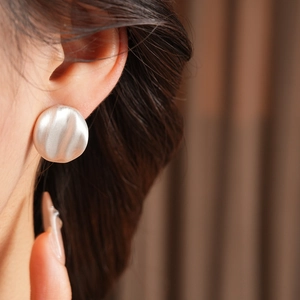 Close-up of large matte silver brushed metal geometric earrings worn by a model
