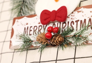 Detailaufnahme von Weihnachtsschild aus Holz mit Schneemann, roter Schleife und Tannenzapfen