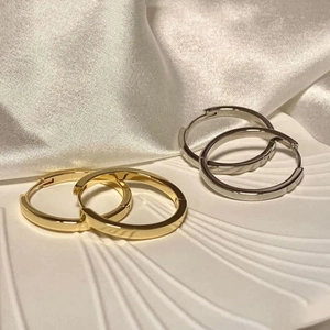 Classic minimalist gold and silver hoop earrings set on white textured tray with silk