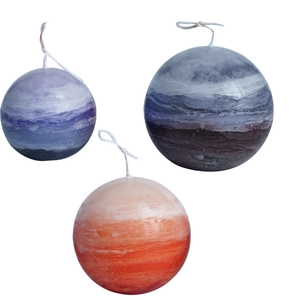 Three spherical planet-textured candles in purple, blue-grey, and orange on white background