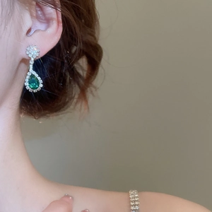 Detail of silver drop earrings featuring a green zircon teardrop and floral halo design