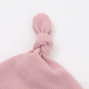 Détail du bonnet en tricot rose pour bébé avec un nœud sur le dessus et texture douce