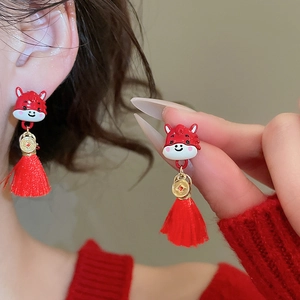 Detailed shot of red enamel ox earrings with gold coin charm and festive silk tassels
