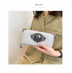 Detail of grey crocodile texture clutch featuring a black metal skull and scroll relief