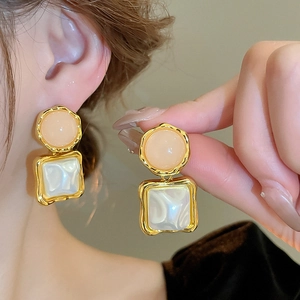 Detail of square faux pearl earrings with peach resin and wavy gold trim
