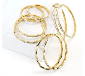 Macro detail of wavy 18K gold hoop earrings with sparkling micro-pave white crystals