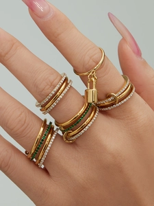 Close-up of stacked gold rings with zircon padlock and green gemstone details