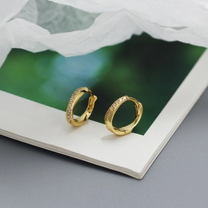 Close-up of gold-plated hoop earrings with crystal pavé on a green magazine backdrop