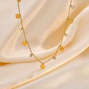 Dettaglio macro di una collana in acciaio dorato con placche tonde e zirconi su seta