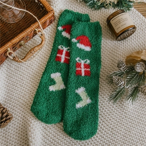Detail of green fluffy Christmas socks with festive patterns on a cozy white blanket