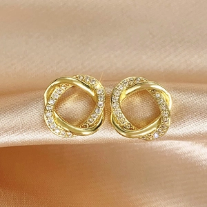 Close-up of gold twisted knot earrings with cubic zirconia on champagne silk background
