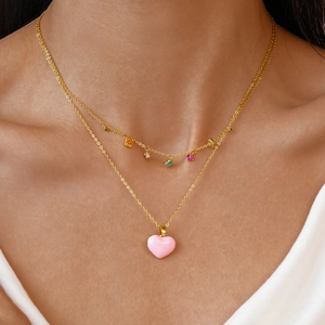 Close-up of layered gold necklaces with pink heart pendant and colorful flower charms