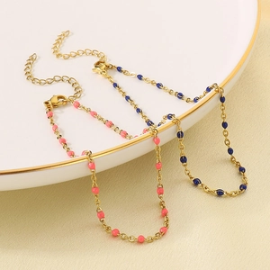 Detail of gold chain anklets with colorful pink and blue enamel beads on a ceramic tray