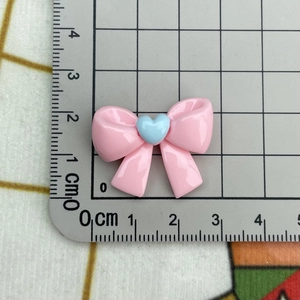 Close-up of pink resin bow with blue heart decoration showing size on grid mat