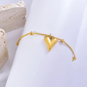 Polished gold heart charm bracelet on a white cylinder with elegant stone background
