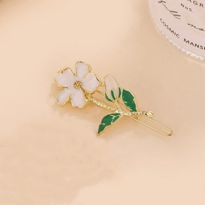 Elegant gold flower hair clip with white enamel petals and green leaves on a warm background