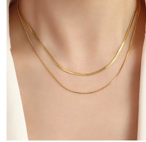 Detail of layered 18k gold plated herringbone and delicate chain necklace on model