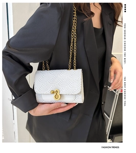 Détail du sac blanc à chaîne avec texture ondulée et fermoir doré sur blazer noir