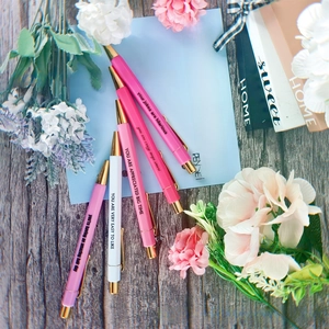 Detailed top-view of five pink and white motivational pens with gold metal accents
